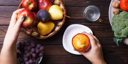 Photo of woman making a decision between fruit and a muffin