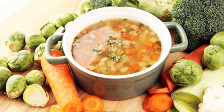 Photo of a bowl of soup with veggies inside. Surrounding the bowl are raw carrots, brussels sprouts, and brocoli