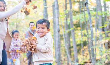Photograph of family with young children playing in fall leaves