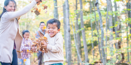Photograph of family with young children playing in fall leaves