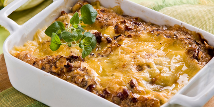 Casserole in a dish topped with melted cheese and fresh herbs