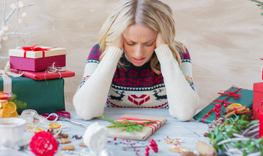 woman in holiday sweater, sitting a table with gifts around her, overwhelmed