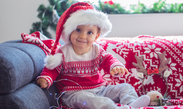 Child holding holiday lights in a red and white sweater and a Santa hat