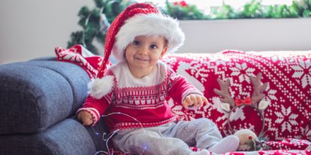 Child holding holiday lights in a red and white sweater and a Santa hat