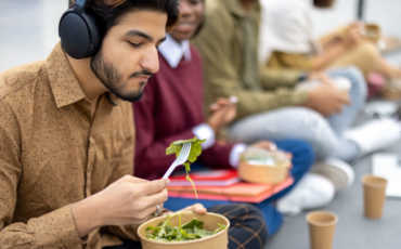 Male college student eating a salad outside among peers
