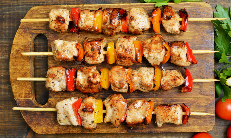 A photo of chicken kebabs layed out on a wooden board.