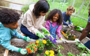 Family planting flowers together outside in a garden bed