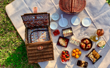 A picnic basket with foods on a picnic blanket