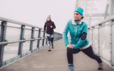 Photo of two women exercising outside during the winter. One is jogging and one is stretching.