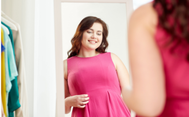 Young woman wearing a pink top looks at her reflection in the mirror, smiling