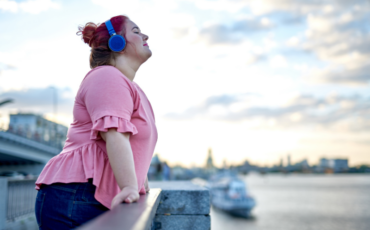 Young adult woman listening to headphones, overlooking the water