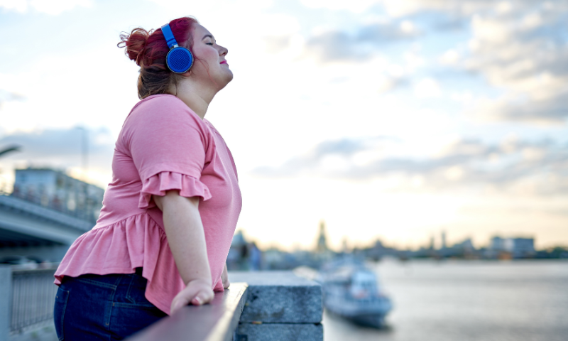 Young adult woman listening to headphones, overlooking the water